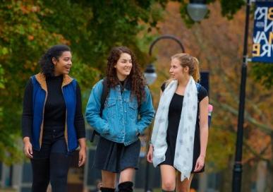 Three students walking on campus with a Bryn Mawr College flag in the background