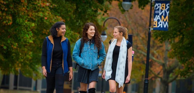 Three students walking on campus with a Bryn Mawr College flag in the background